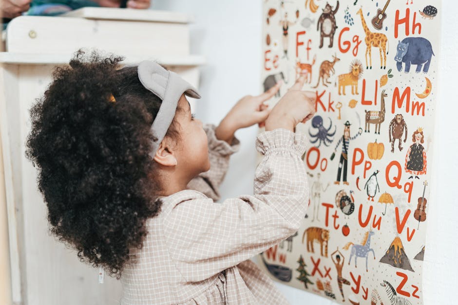 Child with curly hair points to an animal alphabet poster indoors, learning letters and animals