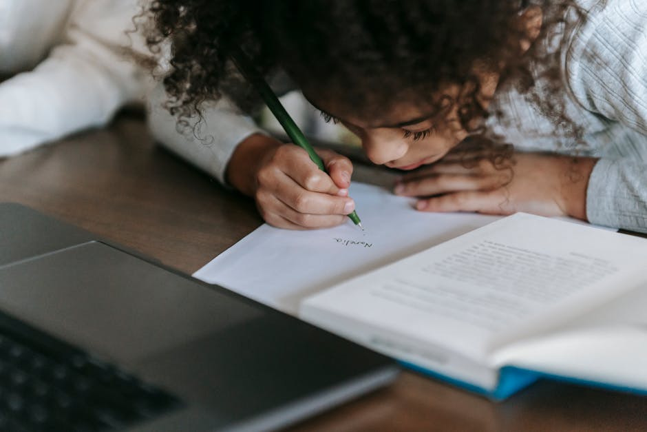 Pensive African American girl with curly hair sitting at table with laptop and book and writing notes on paper while doing homework