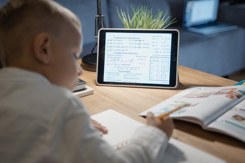 A young boy focuses on math problems on a tablet while studying at a desk indoors