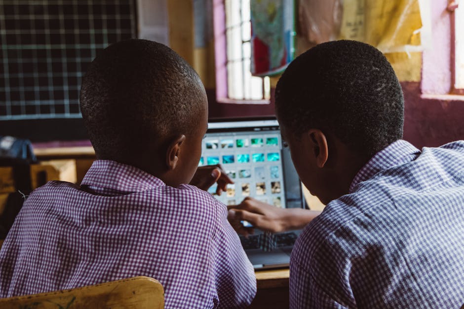 Two schoolchildren in uniform collaborate on a laptop in a classroom setting, focused on learning